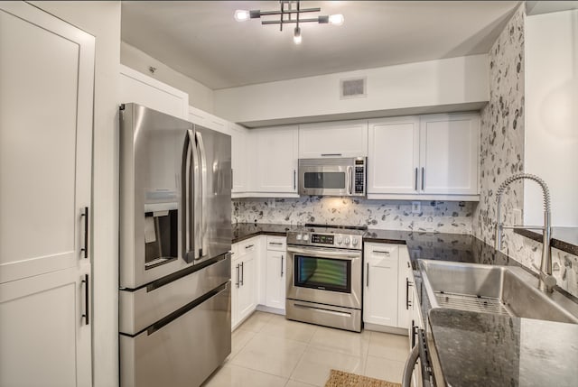 kitchen with dark stone counters, white cabinets, sink, light tile patterned floors, and appliances with stainless steel finishes