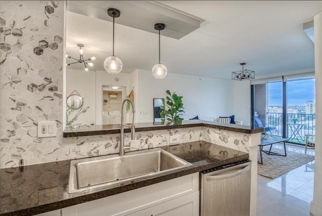 kitchen with stainless steel dishwasher, sink, dark stone countertops, white cabinets, and hanging light fixtures