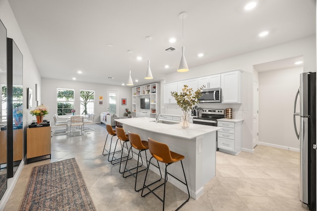 kitchen with sink, stainless steel appliances, a breakfast bar, white cabinets, and a center island with sink