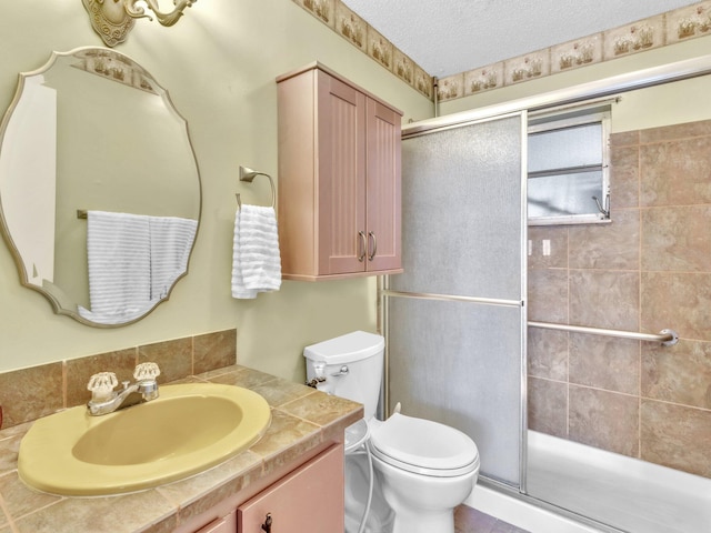 bathroom with vanity, toilet, a shower with door, and a textured ceiling