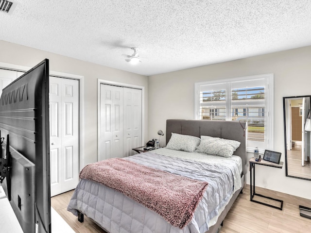 bedroom with a textured ceiling, light hardwood / wood-style flooring, and two closets