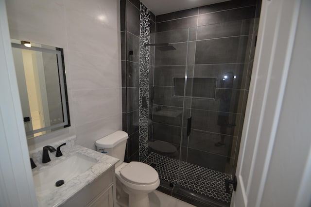 bathroom featuring vanity, toilet, a shower with door, and tile walls