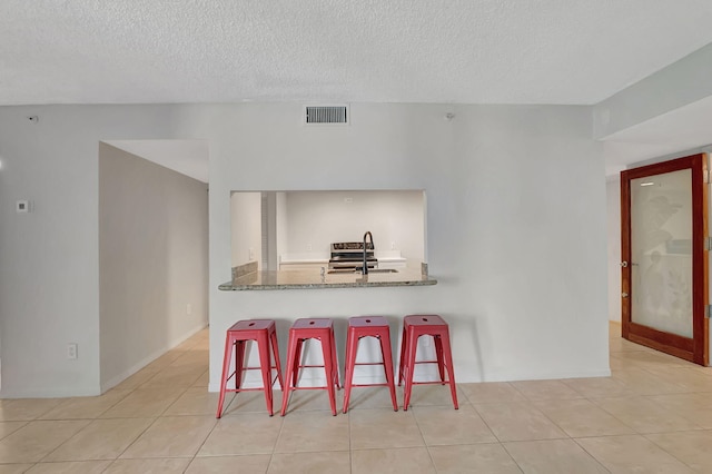 kitchen featuring sink, kitchen peninsula, a textured ceiling, a breakfast bar area, and light tile patterned floors