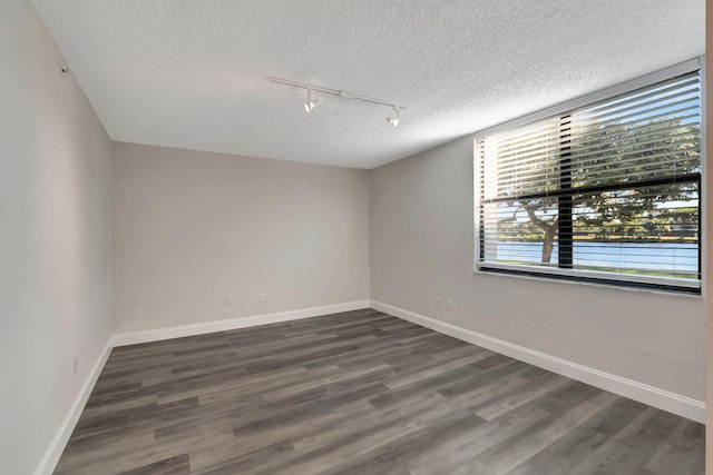 spare room with a textured ceiling, dark hardwood / wood-style floors, and track lighting