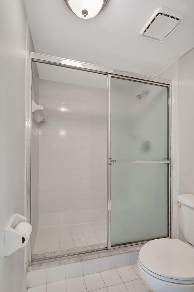 bathroom with tile patterned flooring, toilet, and a shower with door