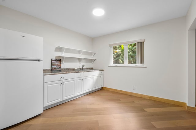 kitchen with white cabinets, freestanding refrigerator, light wood-type flooring, open shelves, and a sink