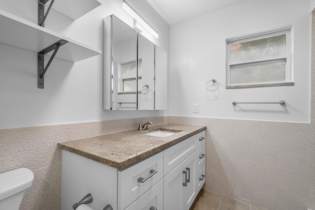 bathroom featuring a wainscoted wall, tile walls, toilet, vanity, and tile patterned floors