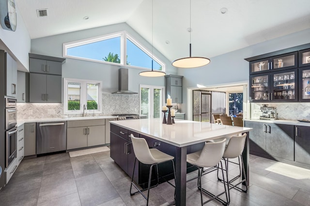 kitchen with a kitchen breakfast bar, wall chimney exhaust hood, pendant lighting, high vaulted ceiling, and a center island