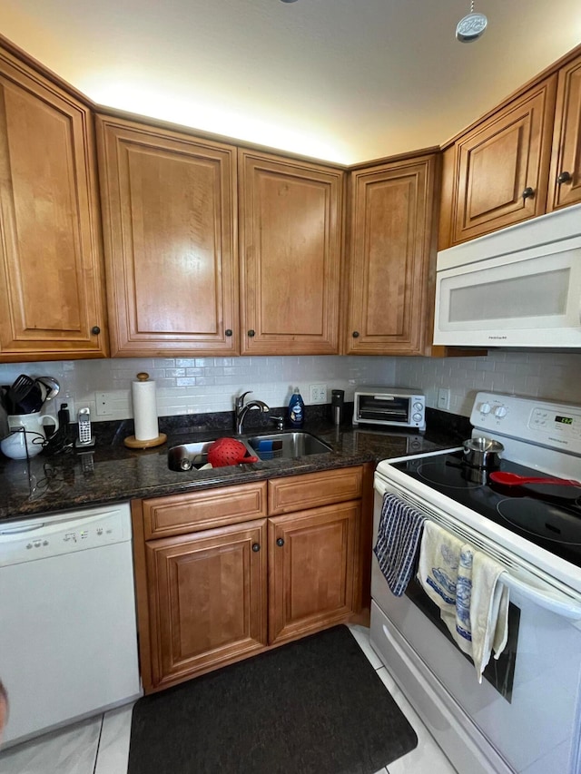 kitchen with dark stone countertops, sink, light tile patterned floors, and white appliances