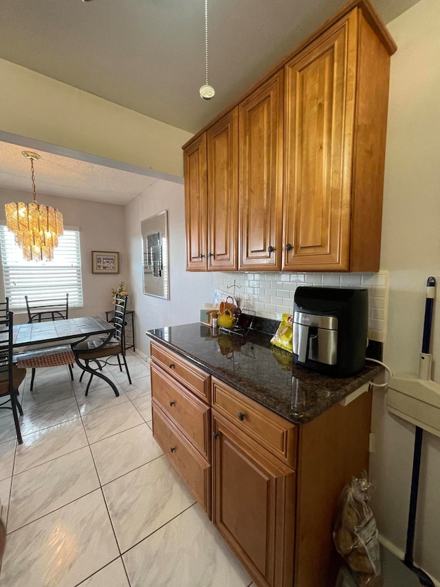 kitchen featuring decorative backsplash, dark stone counters, pendant lighting, light tile patterned floors, and a notable chandelier