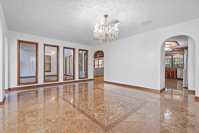 spare room featuring a textured ceiling and a notable chandelier