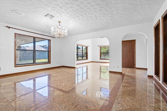 unfurnished room featuring a textured ceiling, plenty of natural light, and a notable chandelier