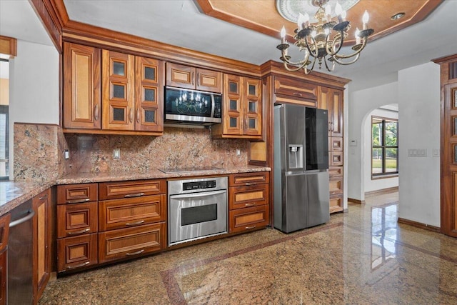 kitchen with backsplash, stainless steel appliances, light stone counters, and a notable chandelier