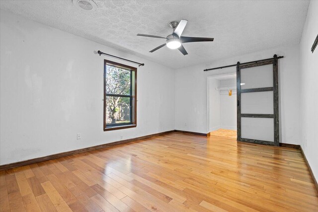 empty room featuring light wood-type flooring, a textured ceiling, a barn door, and ceiling fan