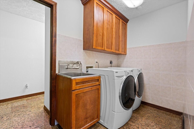 laundry area with cabinets, a textured ceiling, sink, washer and dryer, and tile walls