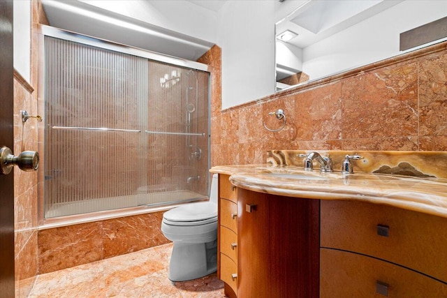 full bathroom with combined bath / shower with glass door, vanity, toilet, and tile walls