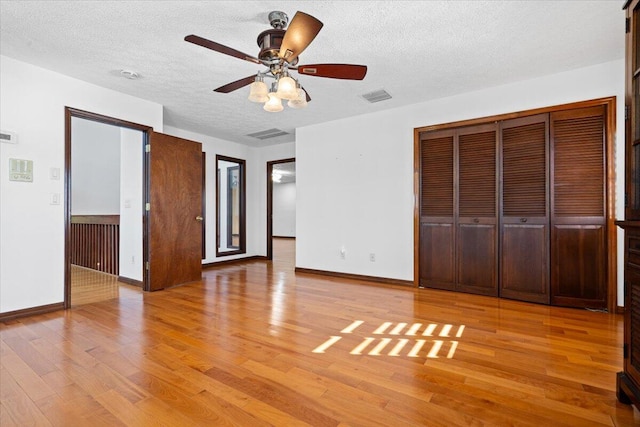 unfurnished bedroom featuring a closet, a textured ceiling, light hardwood / wood-style floors, and ceiling fan