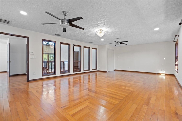 unfurnished room with ceiling fan, a barn door, a textured ceiling, and light hardwood / wood-style flooring