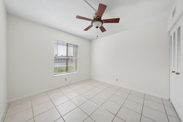 empty room featuring a textured ceiling, ceiling fan, and light tile patterned flooring