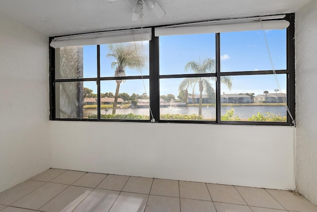 tiled empty room with ceiling fan and a water view