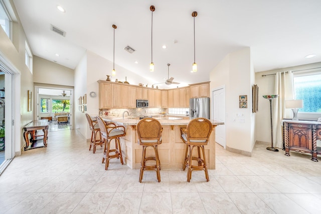 kitchen featuring plenty of natural light, light brown cabinetry, stainless steel appliances, and hanging light fixtures