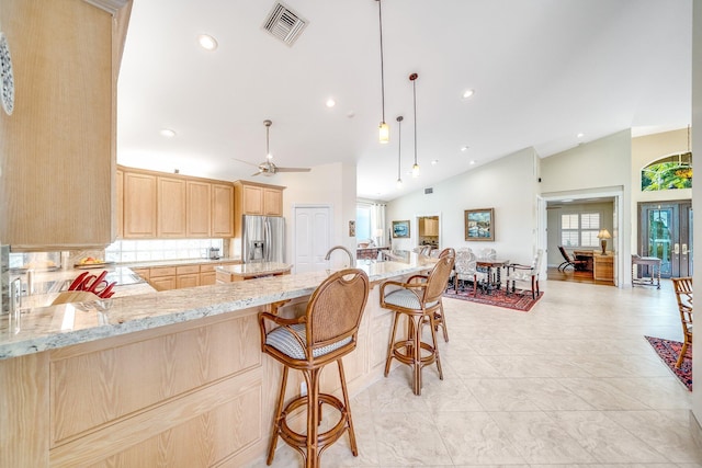 kitchen featuring kitchen peninsula, stainless steel fridge, light brown cabinets, decorative light fixtures, and lofted ceiling