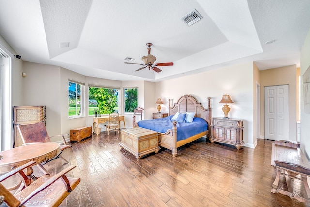 bedroom featuring ceiling fan, wood-type flooring, a textured ceiling, and a tray ceiling