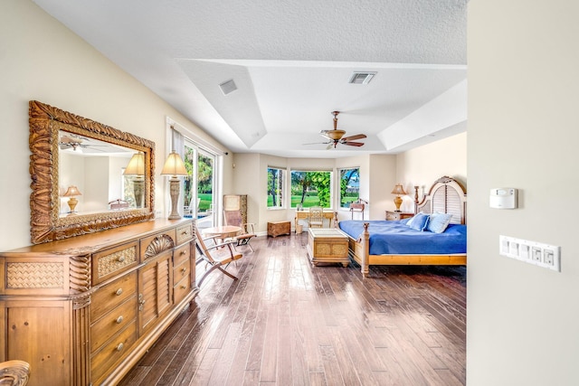 bedroom with a textured ceiling, dark hardwood / wood-style flooring, a raised ceiling, and ceiling fan