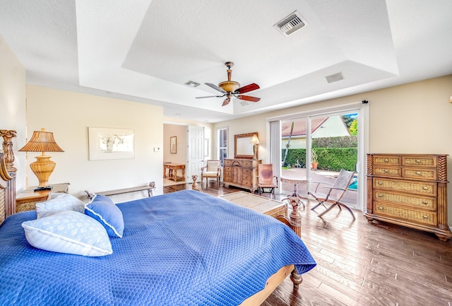 bedroom featuring hardwood / wood-style floors, a raised ceiling, ceiling fan, access to exterior, and a textured ceiling