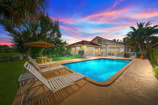 pool at dusk featuring a lawn, a sunroom, and a patio