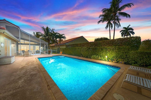 pool at dusk with glass enclosure and a patio area