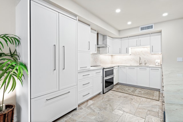 kitchen featuring white cabinetry, double oven range, wall chimney range hood, and sink