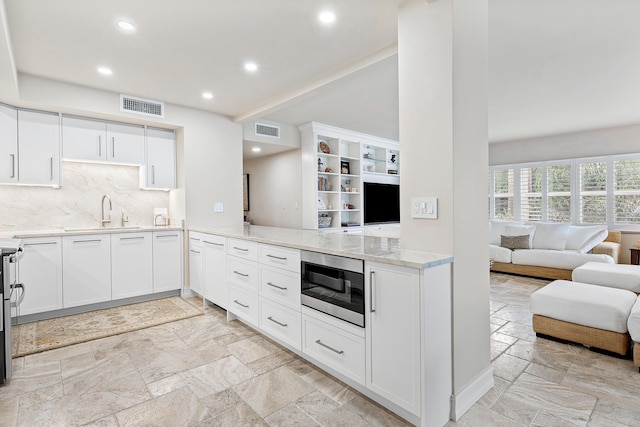 kitchen featuring white cabinetry, built in microwave, sink, tasteful backsplash, and kitchen peninsula