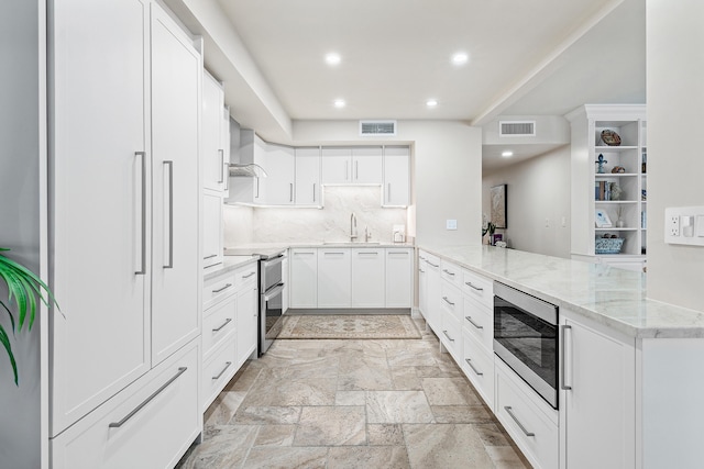 kitchen featuring kitchen peninsula, built in microwave, stainless steel electric stove, wall chimney range hood, and white cabinets