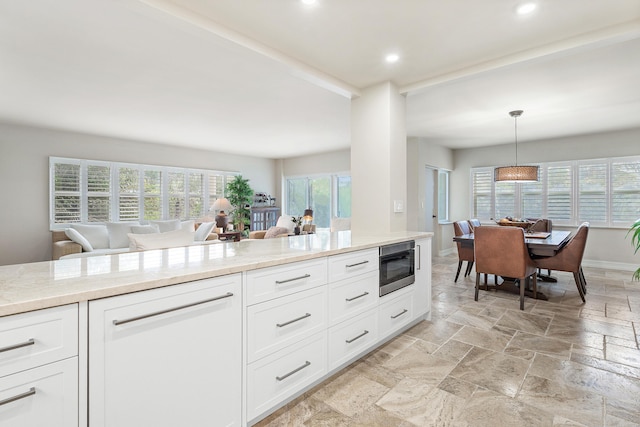 kitchen with white cabinetry, built in microwave, light stone counters, and decorative light fixtures