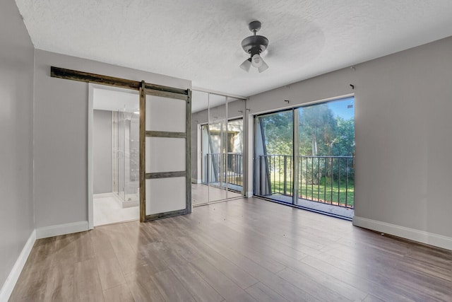 empty room featuring hardwood / wood-style floors, a barn door, a textured ceiling, and ceiling fan