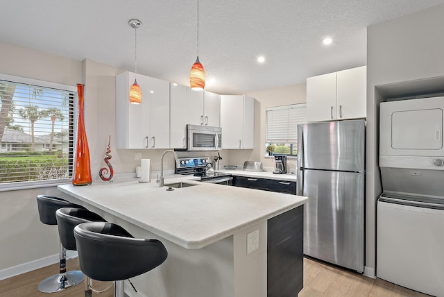 kitchen with stacked washer and clothes dryer, white cabinets, light wood-type flooring, appliances with stainless steel finishes, and decorative light fixtures