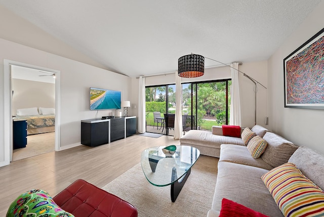 living room with a textured ceiling, light hardwood / wood-style floors, vaulted ceiling, and ceiling fan