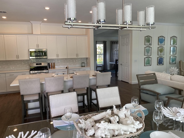 kitchen with pendant lighting, dark wood-type flooring, white cabinets, crown molding, and stainless steel appliances