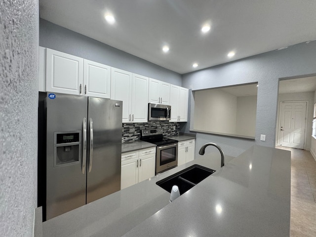 kitchen featuring decorative backsplash, kitchen peninsula, stainless steel appliances, sink, and white cabinetry