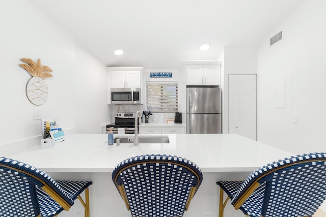 kitchen featuring appliances with stainless steel finishes, white cabinetry, sink, a breakfast bar area, and kitchen peninsula