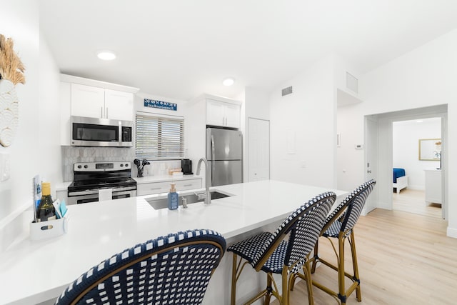 kitchen with sink, stainless steel appliances, light hardwood / wood-style floors, white cabinets, and decorative backsplash