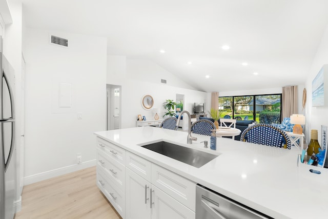 kitchen featuring vaulted ceiling, white cabinetry, sink, light hardwood / wood-style floors, and stainless steel appliances