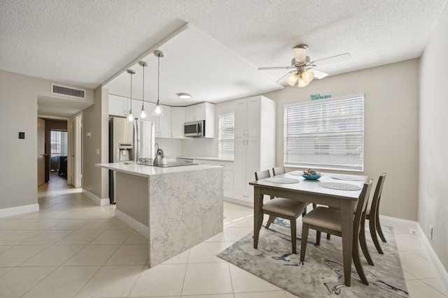 kitchen with pendant lighting, a center island, white cabinets, light tile patterned floors, and appliances with stainless steel finishes