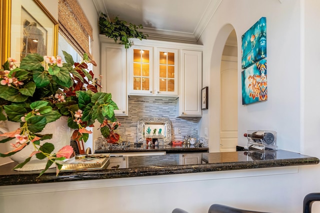 bar with tasteful backsplash, crown molding, white cabinets, and dark stone counters