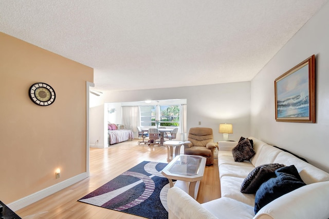 living room featuring light wood-type flooring, baseboards, and a textured ceiling