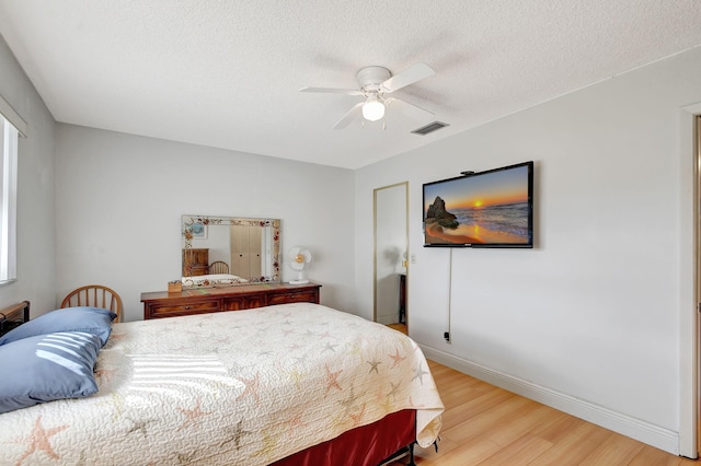 bedroom with a textured ceiling, a ceiling fan, visible vents, baseboards, and light wood finished floors