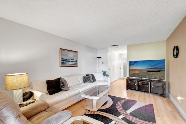 living room with light wood-type flooring, baseboards, and a textured ceiling