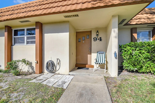 property entrance with visible vents, a tiled roof, and stucco siding