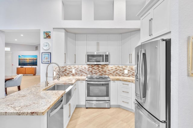 kitchen with lofted ceiling, white cabinets, sink, light stone counters, and stainless steel appliances